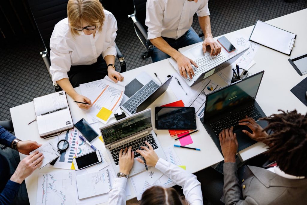 Vibrant office teamwork scene with laptops, documents, and diverse professionals in a meeting.