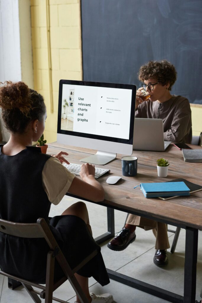 Two adults in an office discussing data on a computer screen.